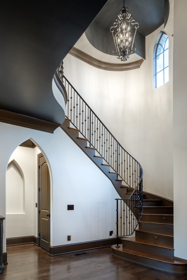 staircase featuring wood-type flooring, a high ceiling, and a notable chandelier