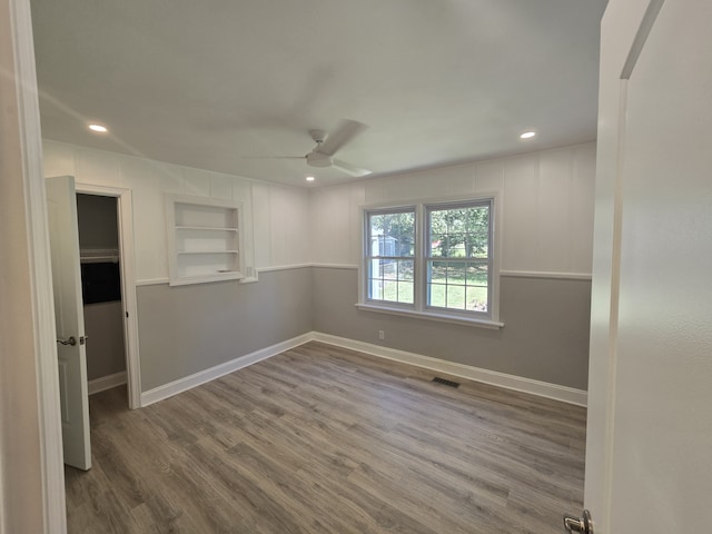 unfurnished room with built in shelves, hardwood / wood-style floors, and ceiling fan