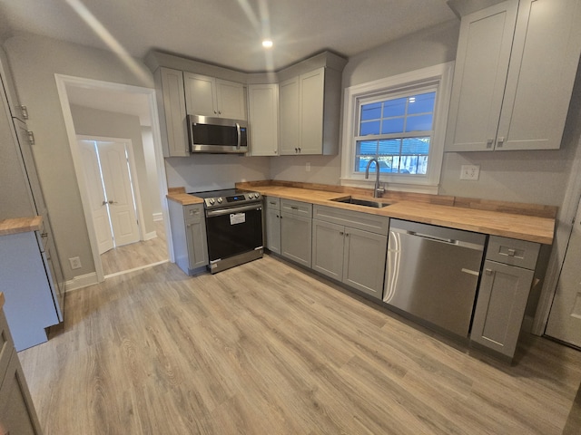 kitchen featuring stainless steel appliances, sink, wooden counters, and light hardwood / wood-style flooring