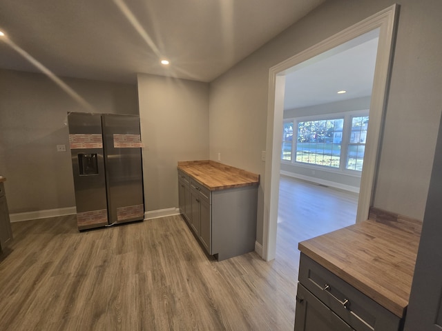 kitchen with light wood-type flooring, stainless steel fridge with ice dispenser, and butcher block counters