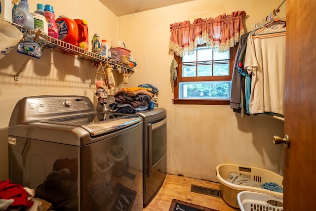 laundry area featuring light wood-type flooring, a textured ceiling, and washing machine and dryer