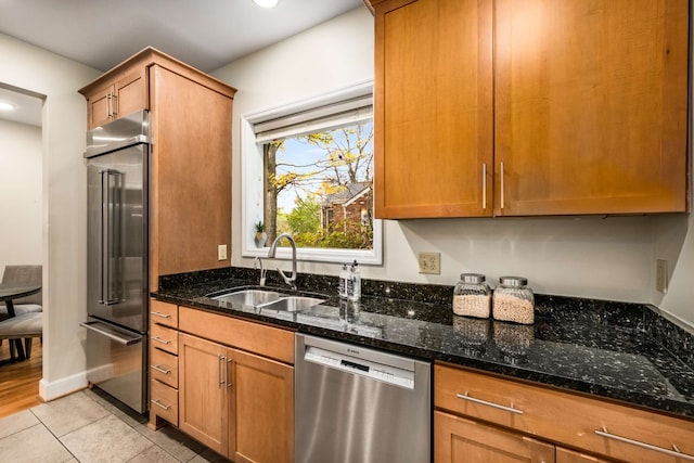 kitchen with dark stone countertops, sink, light tile patterned floors, and stainless steel appliances