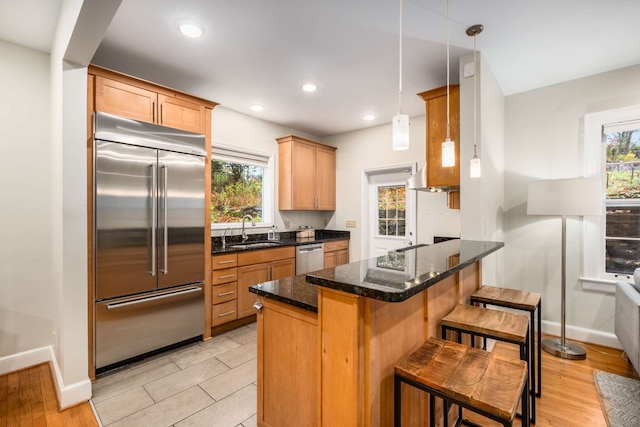 kitchen with appliances with stainless steel finishes, a breakfast bar, a healthy amount of sunlight, sink, and decorative light fixtures