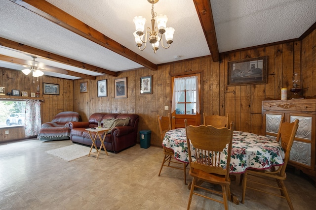 dining room with ceiling fan with notable chandelier, wooden walls, a textured ceiling, and plenty of natural light