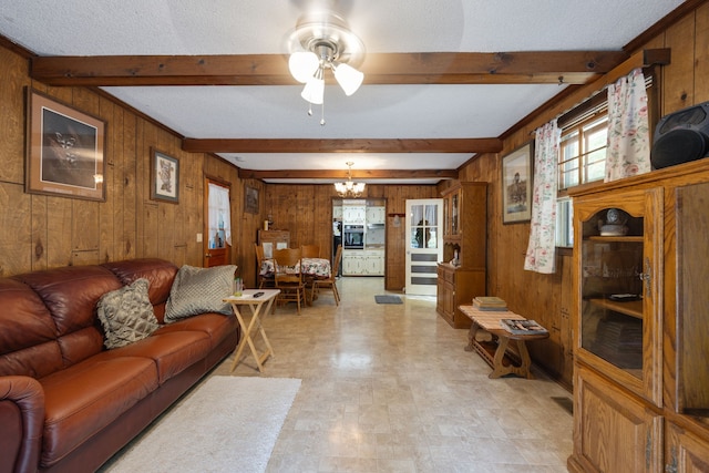 living room with ceiling fan with notable chandelier, beam ceiling, wood walls, and a textured ceiling