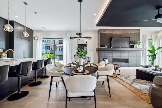 dining area featuring ceiling fan, light wood finished floors, a tiled fireplace, and recessed lighting