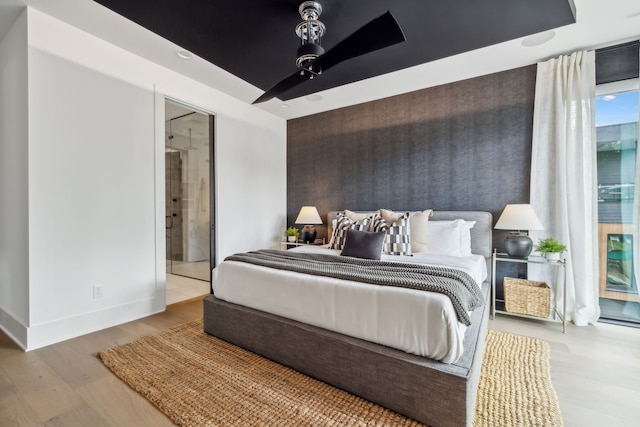 bedroom featuring baseboards, a ceiling fan, connected bathroom, an accent wall, and wood finished floors