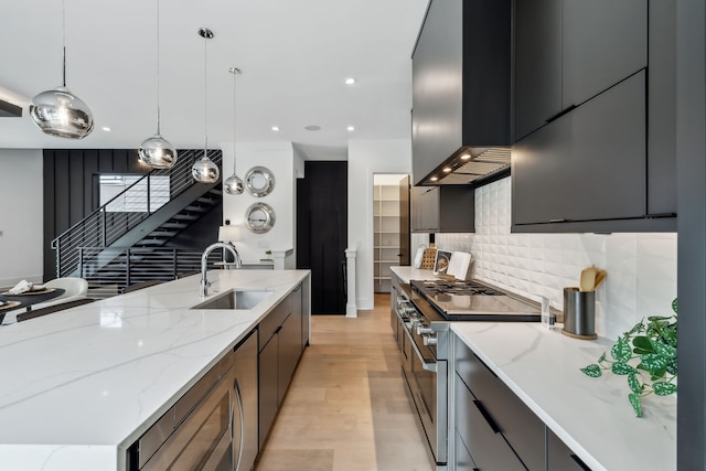 kitchen with backsplash, appliances with stainless steel finishes, a sink, modern cabinets, and wall chimney exhaust hood