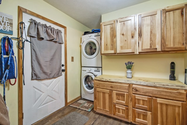 clothes washing area featuring cabinets, stacked washer / dryer, and dark hardwood / wood-style floors