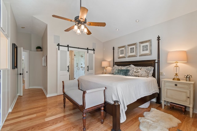 bedroom with light hardwood / wood-style flooring, a barn door, ceiling fan, and vaulted ceiling