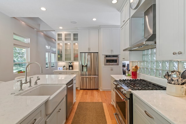 kitchen featuring light stone countertops, wall chimney range hood, light wood-type flooring, and appliances with stainless steel finishes