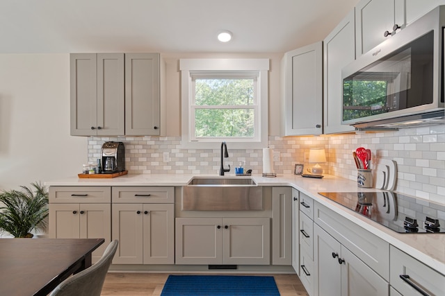 kitchen featuring black electric cooktop, sink, backsplash, and light hardwood / wood-style flooring