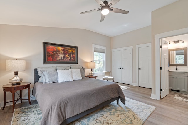 bedroom with light wood-type flooring, vaulted ceiling, ceiling fan, and ensuite bathroom