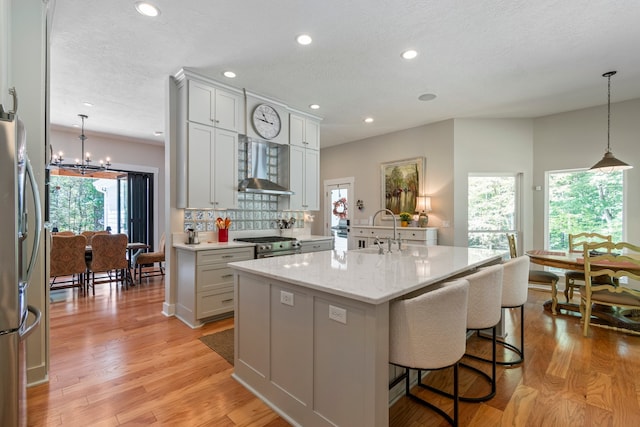 kitchen featuring a center island with sink, plenty of natural light, sink, and wall chimney range hood