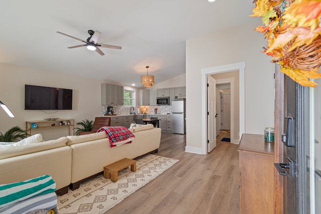 living room with ceiling fan, sink, light hardwood / wood-style flooring, and vaulted ceiling