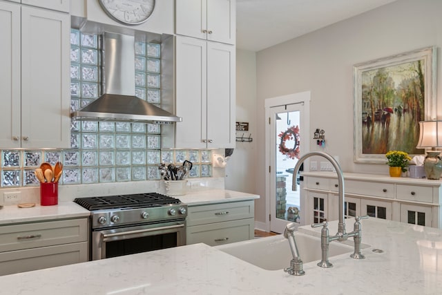 kitchen featuring light stone countertops, wall chimney exhaust hood, sink, and stainless steel range