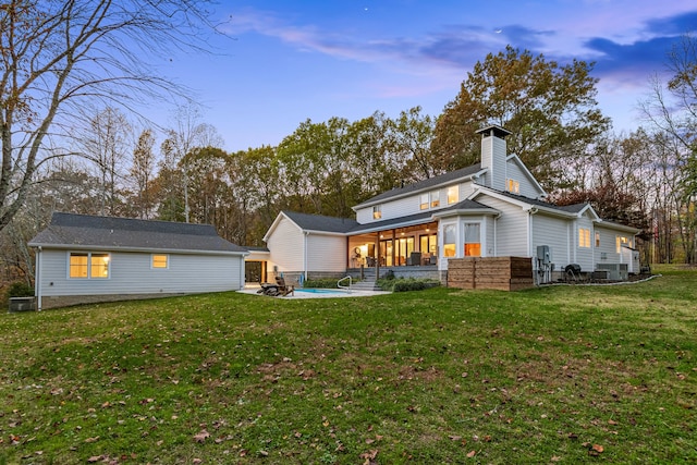 back house at dusk with a patio, a sunroom, a yard, and cooling unit