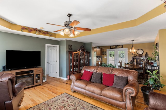 living room featuring ceiling fan with notable chandelier, light hardwood / wood-style floors, and a tray ceiling