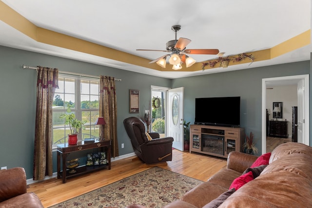 living room featuring ceiling fan, a tray ceiling, and light hardwood / wood-style floors