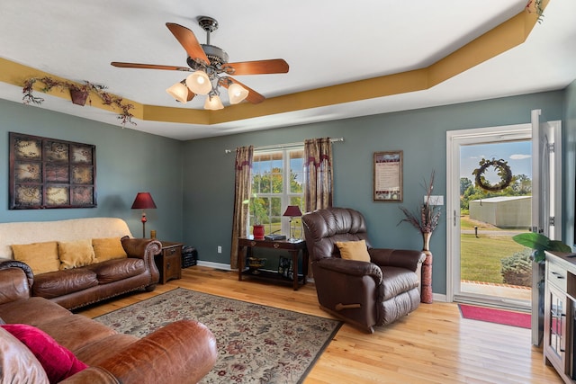 living room featuring light wood-type flooring, ceiling fan, and a raised ceiling