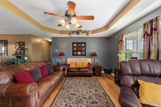 living room with a raised ceiling, light hardwood / wood-style floors, and ceiling fan