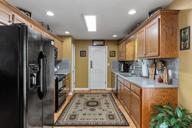 kitchen featuring light wood-type flooring, sink, tasteful backsplash, and black appliances