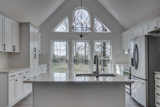 kitchen featuring stainless steel refrigerator with ice dispenser, white cabinetry, light stone countertops, and sink