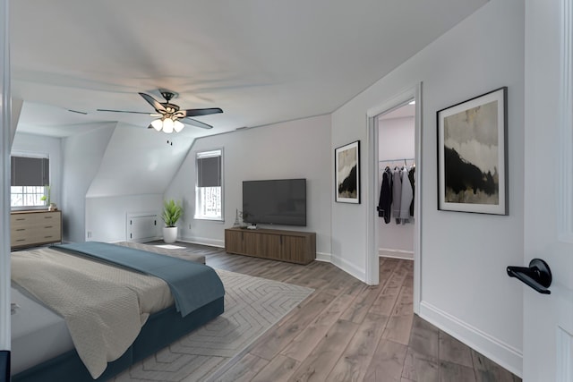 bedroom with light hardwood / wood-style floors, a closet, vaulted ceiling, a spacious closet, and ceiling fan