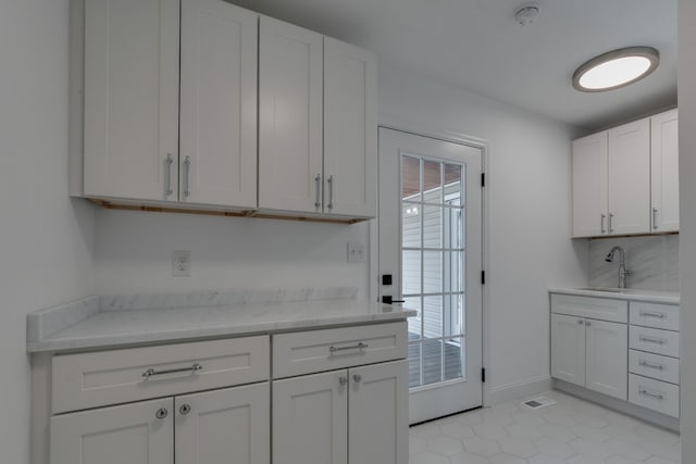 kitchen with white cabinetry, light stone counters, light tile patterned flooring, and sink