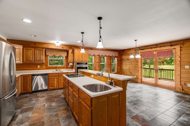 kitchen featuring appliances with stainless steel finishes, a center island with sink, wood walls, and plenty of natural light