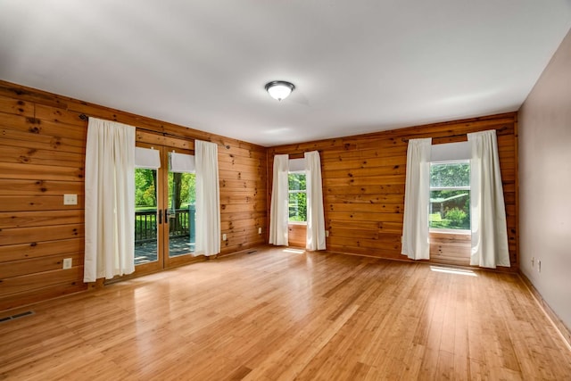 unfurnished room with a healthy amount of sunlight, light hardwood / wood-style floors, and wooden walls