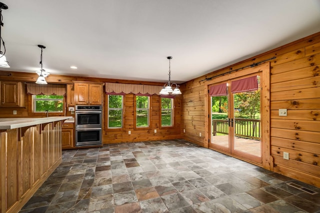 kitchen with wooden walls, decorative light fixtures, double oven, and a healthy amount of sunlight