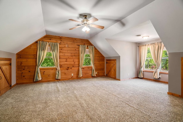 bonus room with wooden walls, carpet, ceiling fan, and plenty of natural light