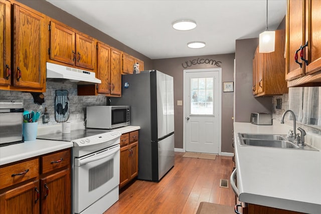 kitchen featuring appliances with stainless steel finishes, hanging light fixtures, decorative backsplash, light hardwood / wood-style flooring, and sink