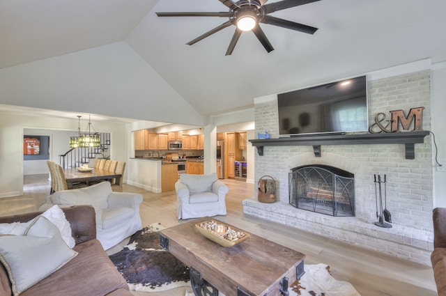 living room with a fireplace, light hardwood / wood-style flooring, high vaulted ceiling, and ceiling fan with notable chandelier