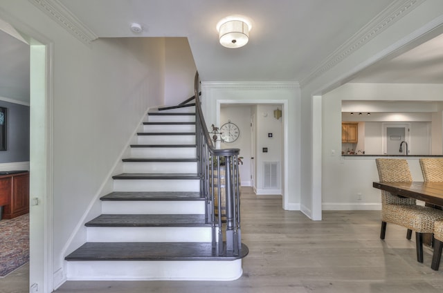 staircase featuring hardwood / wood-style flooring, sink, and crown molding