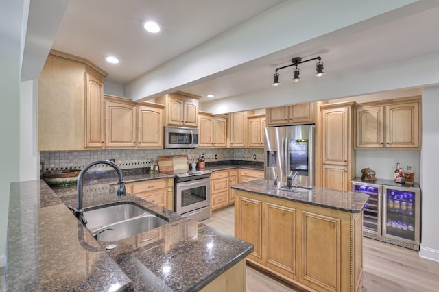 kitchen with light wood-type flooring, stainless steel appliances, beverage cooler, sink, and dark stone countertops