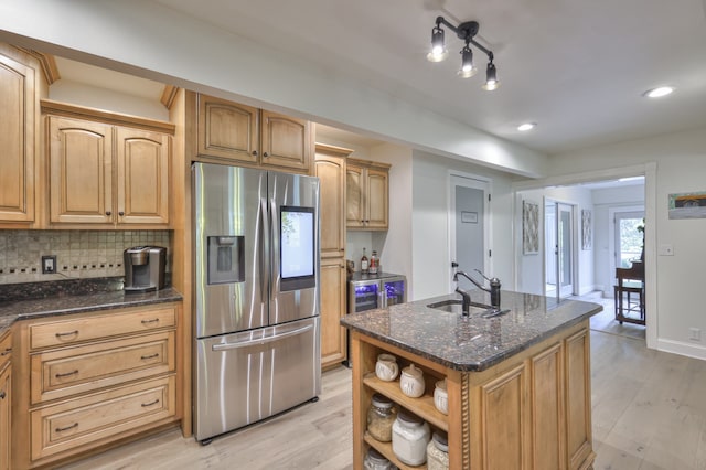 kitchen featuring a kitchen island with sink, dark stone counters, sink, stainless steel refrigerator with ice dispenser, and light hardwood / wood-style floors