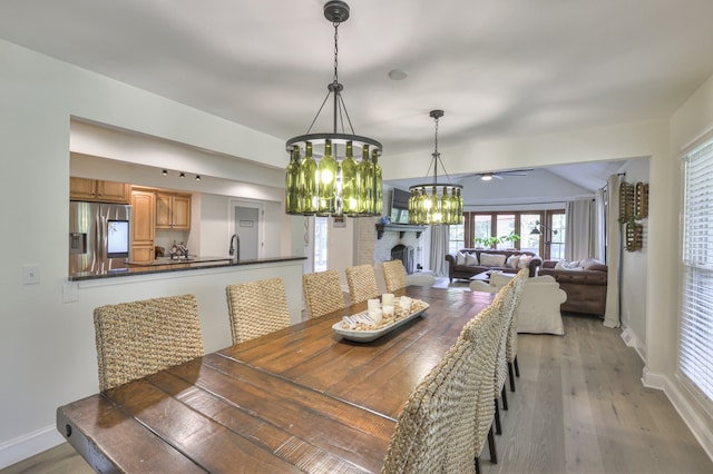 dining area with sink, ceiling fan with notable chandelier, and light wood-type flooring