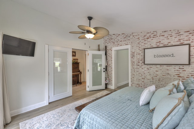 bedroom featuring ceiling fan, light hardwood / wood-style flooring, brick wall, and lofted ceiling