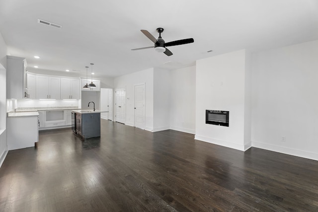 unfurnished living room with heating unit, ceiling fan, dark hardwood / wood-style floors, and sink