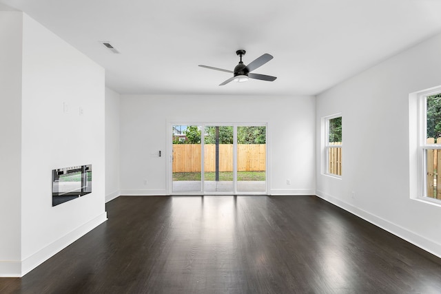 unfurnished living room with heating unit, dark wood-type flooring, ceiling fan, and a wealth of natural light