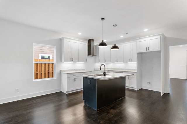 kitchen featuring wall chimney exhaust hood, white cabinetry, a center island with sink, and hanging light fixtures