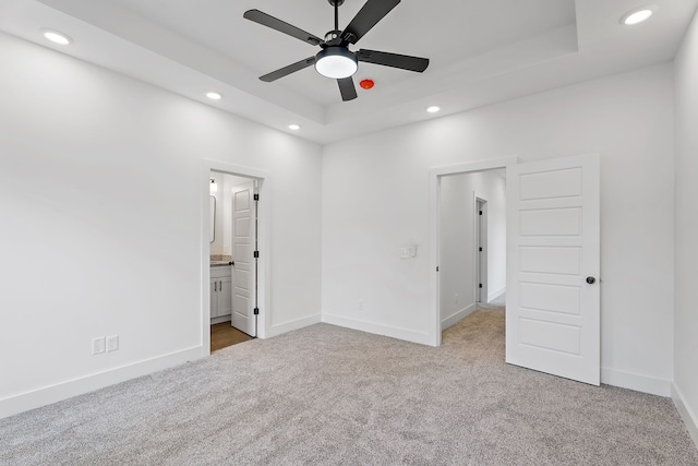 unfurnished bedroom featuring a tray ceiling, ceiling fan, light colored carpet, and ensuite bathroom