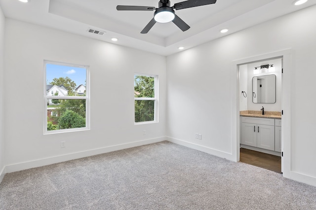 unfurnished bedroom featuring carpet floors, a raised ceiling, ceiling fan, ensuite bathroom, and sink