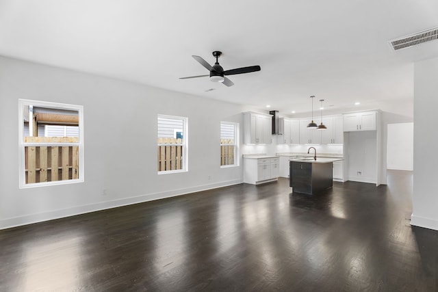 unfurnished living room featuring ceiling fan, sink, plenty of natural light, and dark wood-type flooring