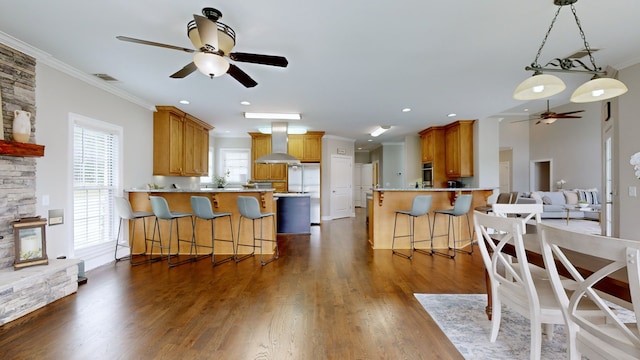 kitchen featuring island exhaust hood, kitchen peninsula, ceiling fan, and a breakfast bar