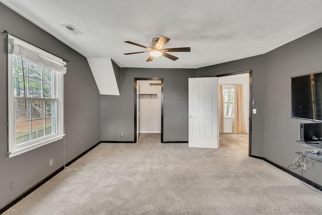 unfurnished bedroom featuring multiple windows, a walk in closet, light colored carpet, and a textured ceiling