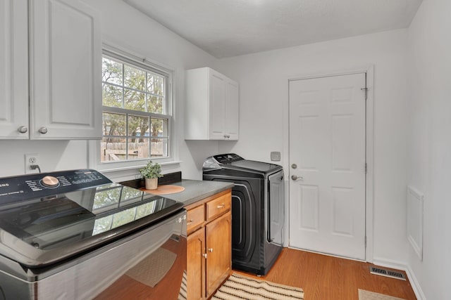 clothes washing area featuring washer and dryer, cabinets, and light hardwood / wood-style flooring