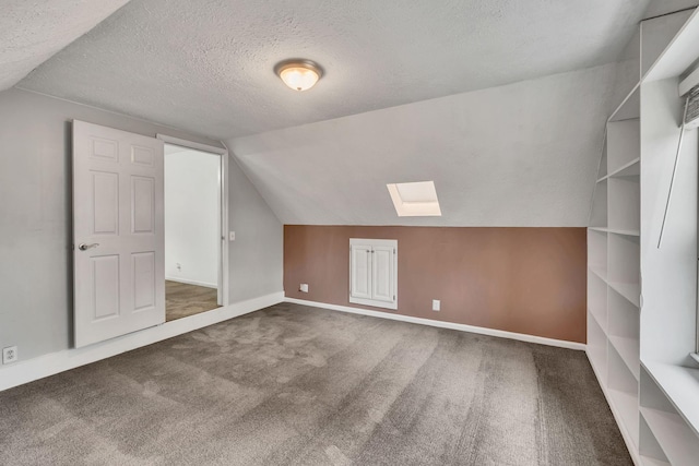 bonus room featuring lofted ceiling with skylight, dark carpet, and a textured ceiling